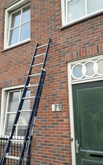Ladder tegen een bakstenen gevel met wit geschilderde kozijnen en een groene voordeur