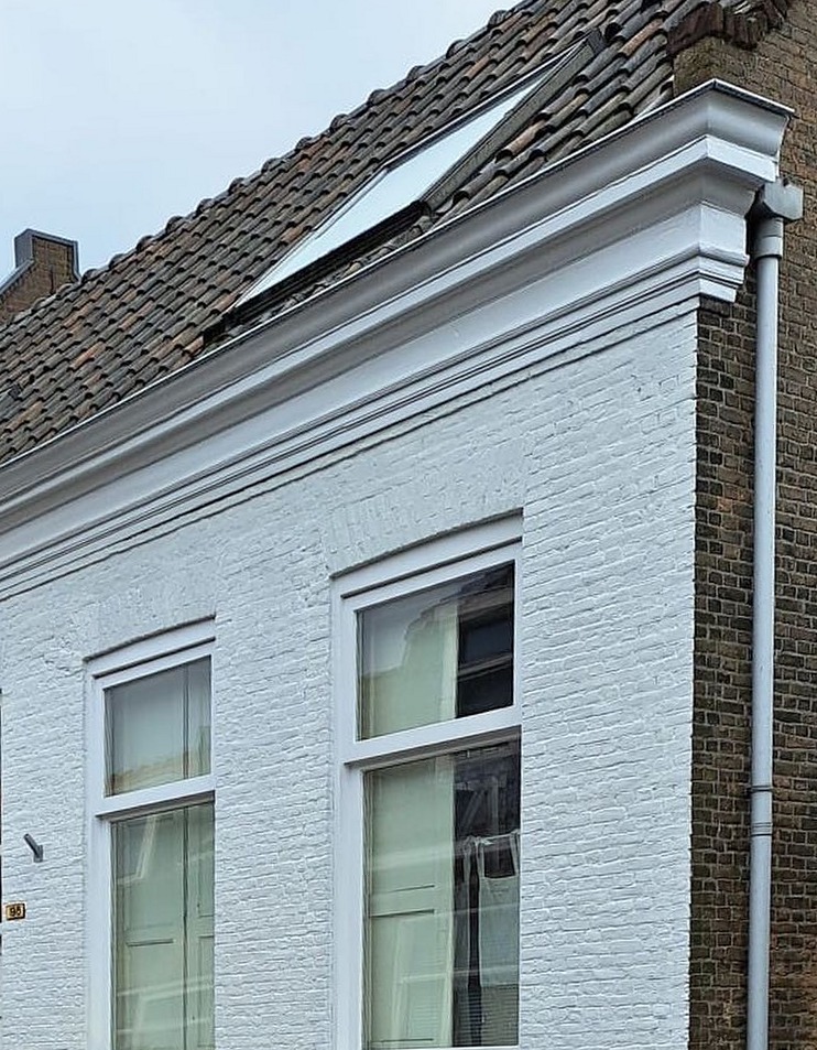 Wit geschilderde bakstenen voorgevel met witte kozijnen en kroonlijst, naast een ongeschilderde buurgevel